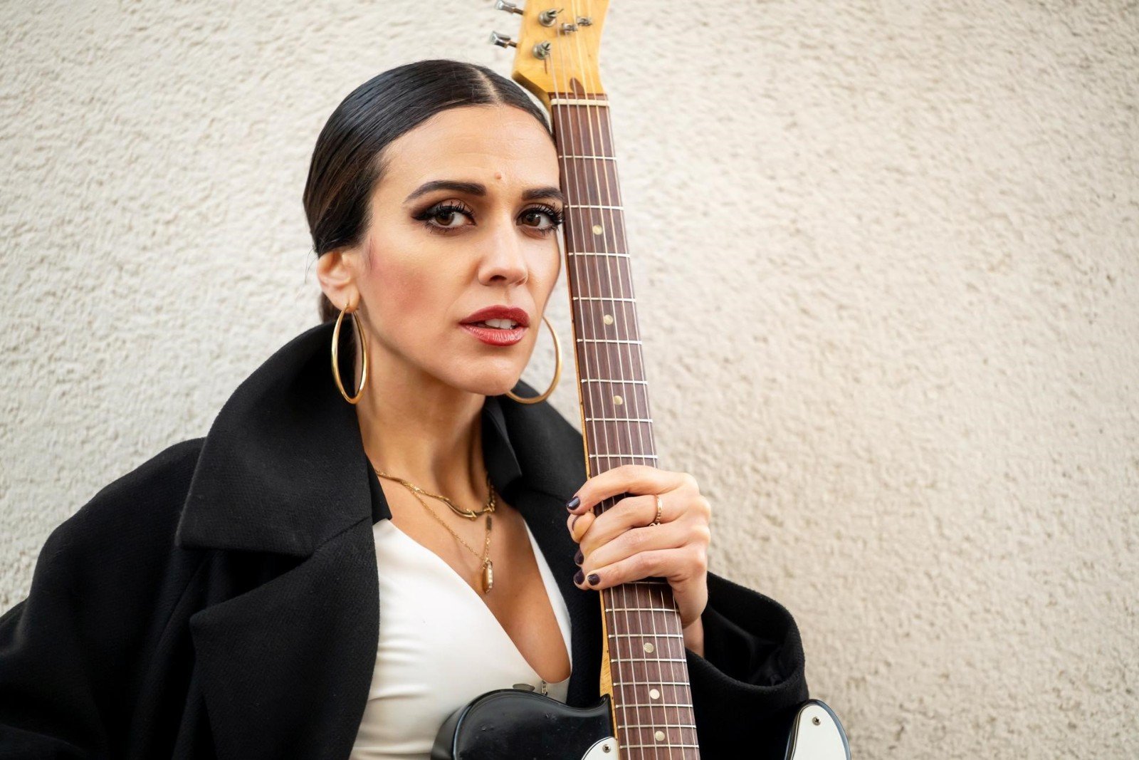 Eleonora Strino con una chitarra elettrica appoggiata sulla spalla, davanti a un muro chiaro
