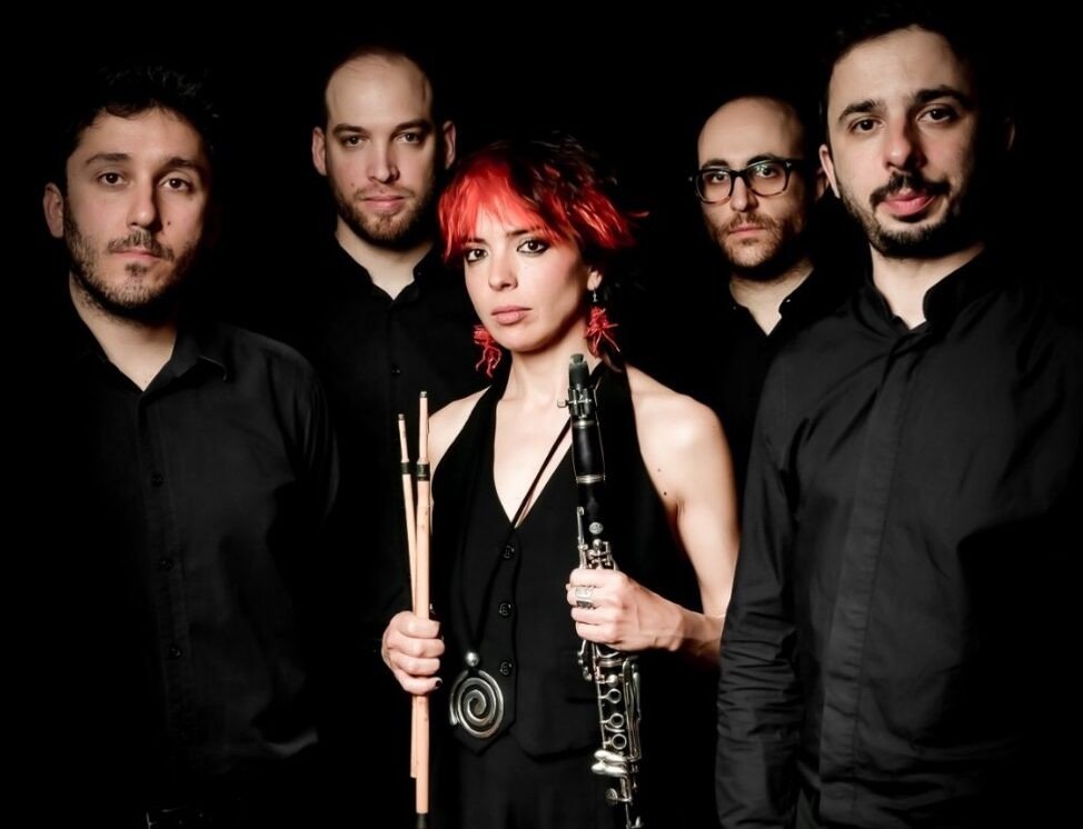 Foto di Zoe Pia con il clarinetto insieme ai quattro musicisti dell'EIC Eden Inverted Collective, tutti vestiti di nero su fondo scuro